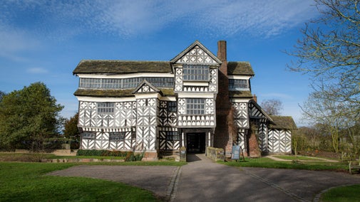 Exterior of the iconic wood frame moated Tudor manor house with black and white features and a blue sky in the background